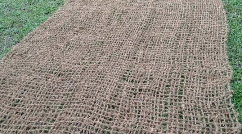 A natural jute garden erosion control mat unrolled on a green lawn, showcasing its eco-friendly mesh