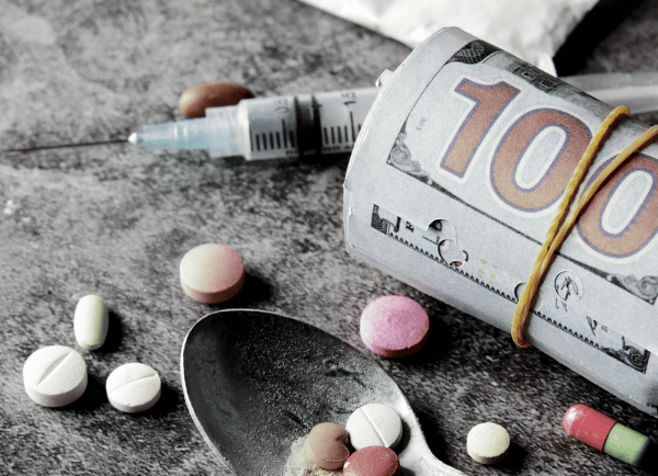 a spoon has tablets and a syringe and a bundle of cash