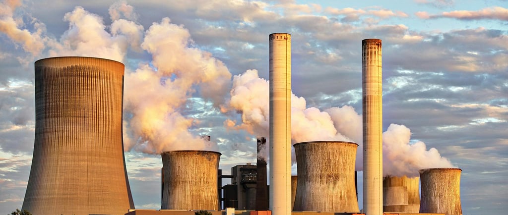 An industrial power plant with multiple cooling towers and smokestacks emitting white smoke into the