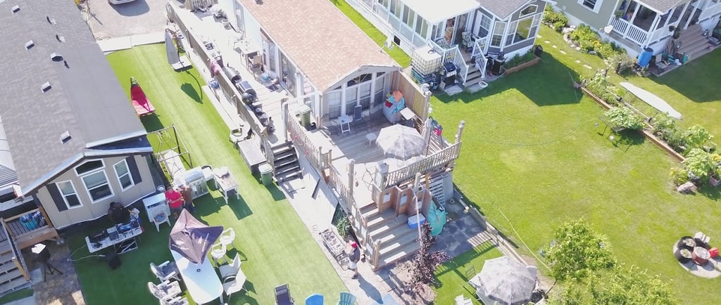 Aerial view of a vacation resort featuring modular mobile homes with large wooden decks and green lawns.