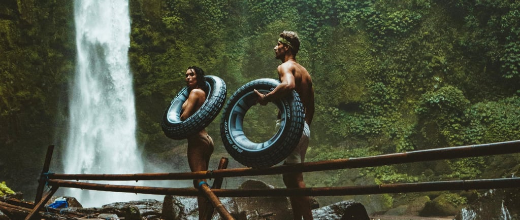 a woman and a man standing on a bridge by a waterfall holding inner tubes