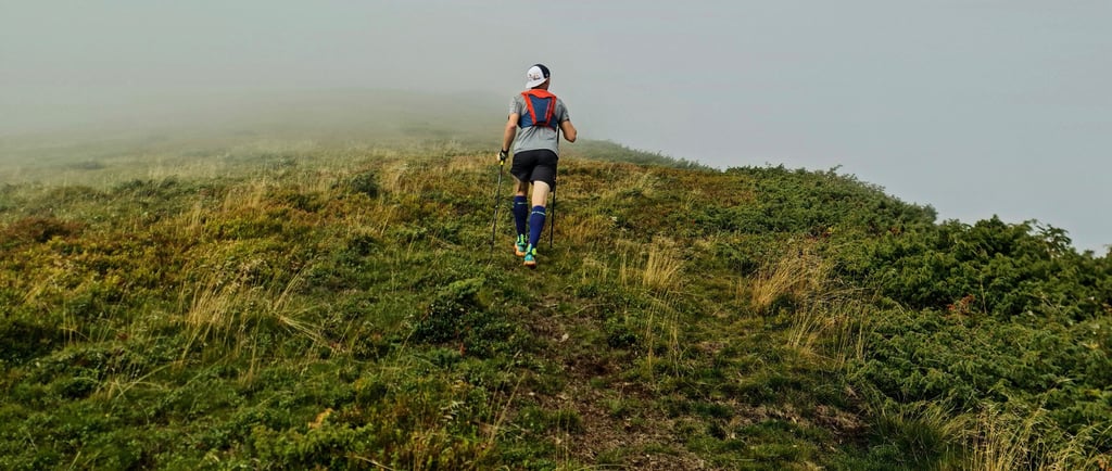 a man hiking on a misty hill wearing a backpack using hiking poles