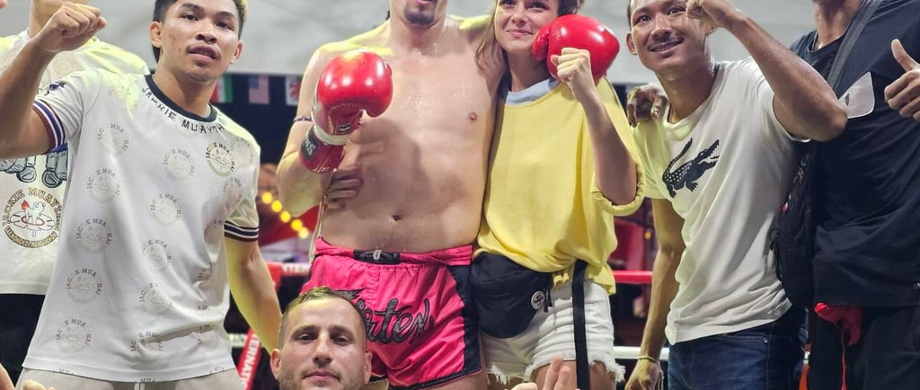 A victorious Muay Thai fighter in red gloves and pink shorts poses with his team in a boxing ring.