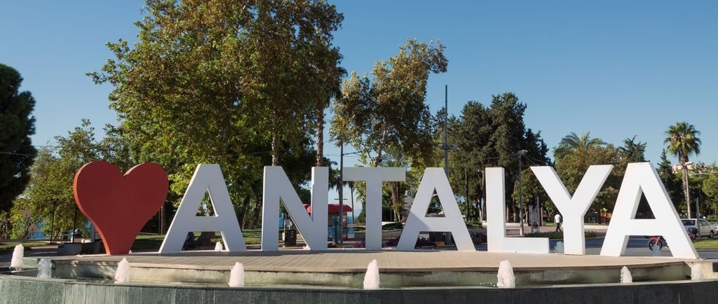 Praça em Antália com o letreiro da cidade ao fundo.