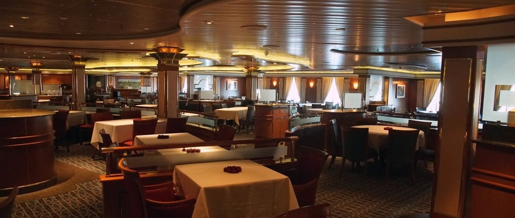 Restaurante elegante a bordo de navio de cruzeiro, com mesas arrumadas, iluminação suave.