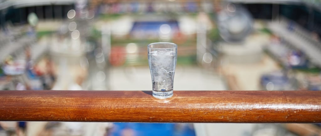 Copo de água sobre o deck do navio com vista para o mar, destacando bebidas e segurança a bordo