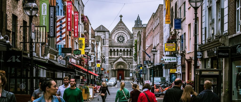 Rua movimentada no centro de Dublin com pedestres e comércio local.