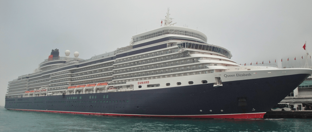 Navio Queen Elizabeth ancorado no porto de Hong Kong, com a cidade ao fundo.