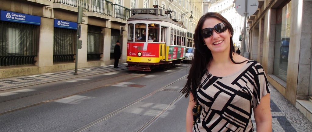 Foto da autora no centro de Lisboa em frente ao Elétrico 28 passando ao fundo