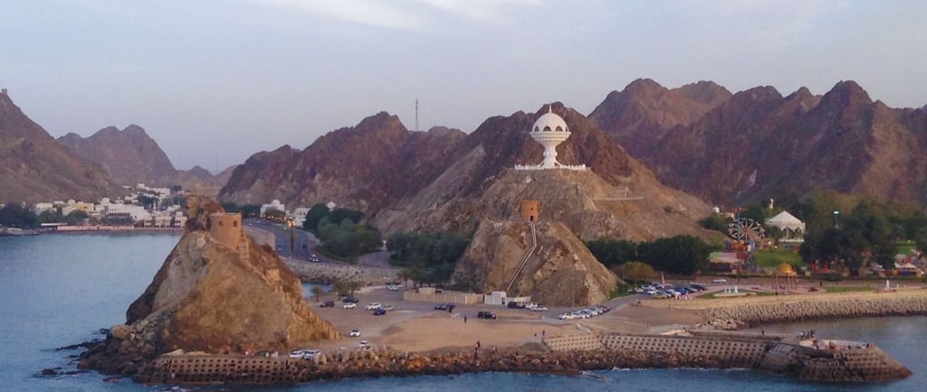 Vista do porto de Muscat com montanhas ao fundo, chegando de navio ao amanhecer.