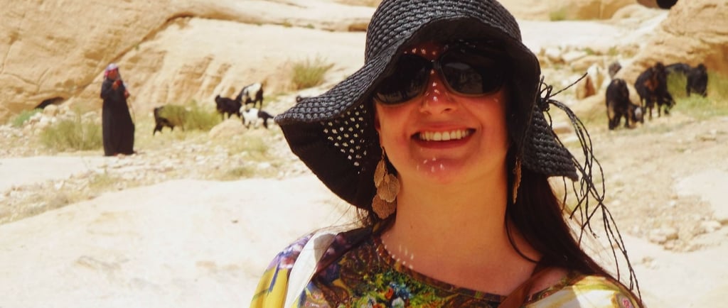 Autora saindo de Petra, com uma família beduína ao fundo, em meio às formações rochosas e ao cenário