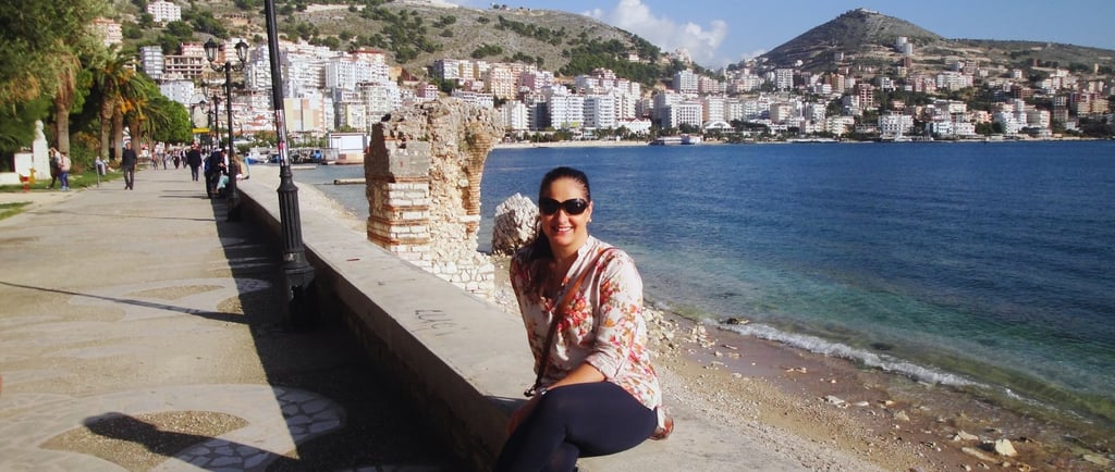 Autora sentada no píer de Sarandë, contemplando a paisagem tranquila da costa albanesa.