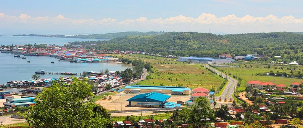 Panorama do porto de Sihanoukville com a cidade ao fundo, entre o mar e o céu.