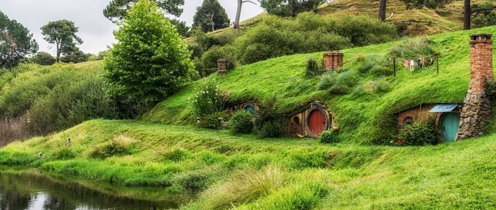Vista de Hobbiton Village, mostrando as casas temáticas, jardins e paisagens verdes ao redor.