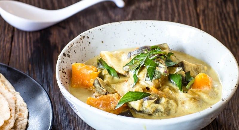 Vegetable curry in a bowl topped with spinach leaves. A side of paratha just out of frame.