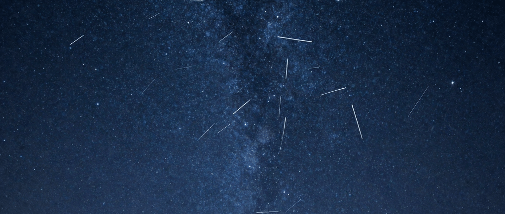 A vibrant meteor shower streaks across the dark night sky over a silhouette of a single tree and the Milky Way galaxy.