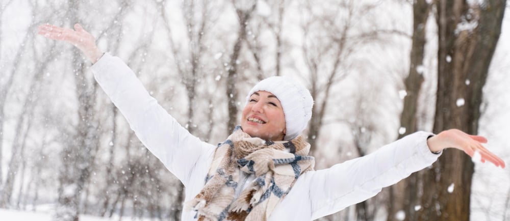 femme avec bonnet et echarpe dans la neige qui sourit