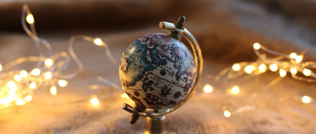 Vintage mini globe on a brass stand surrounded by warm fairy lights on a brown blanket.