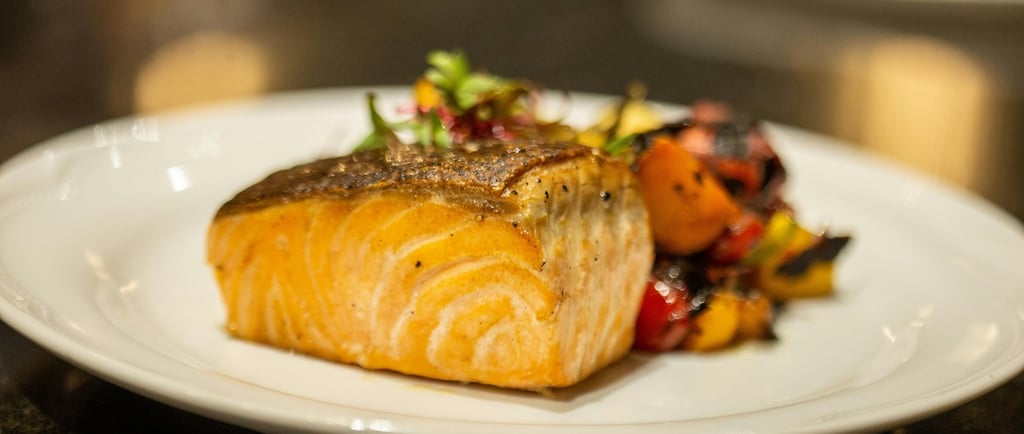 Pan-seared Atlantic salmon fillet served with roasted Mediterranean vegetables on a white plate.