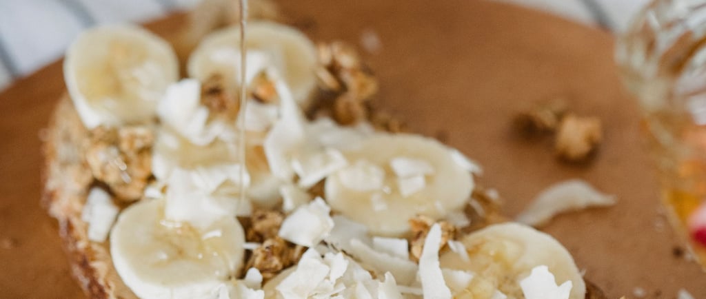 Drizzling honey over healthy sourdough toast topped with sliced bananas, coconut flakes, and granola.