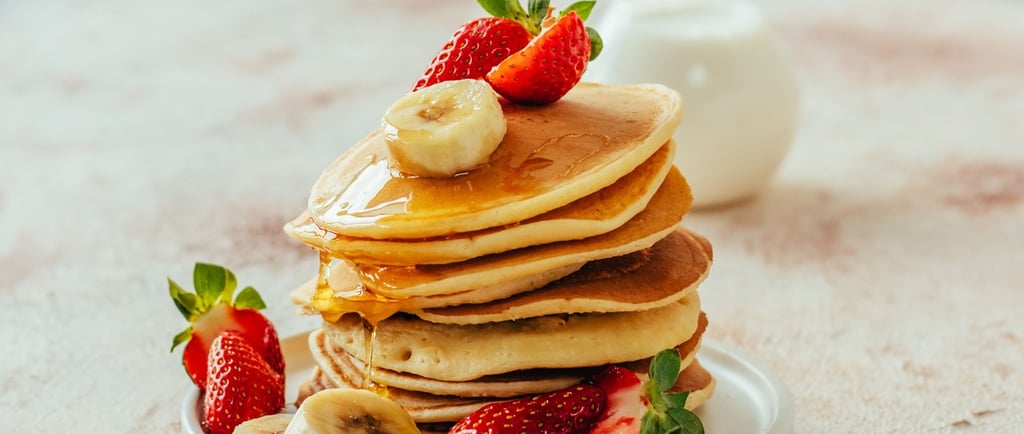 Stack of fluffy buttermilk pancakes topped with maple syrup, fresh strawberries, and banana slices.
