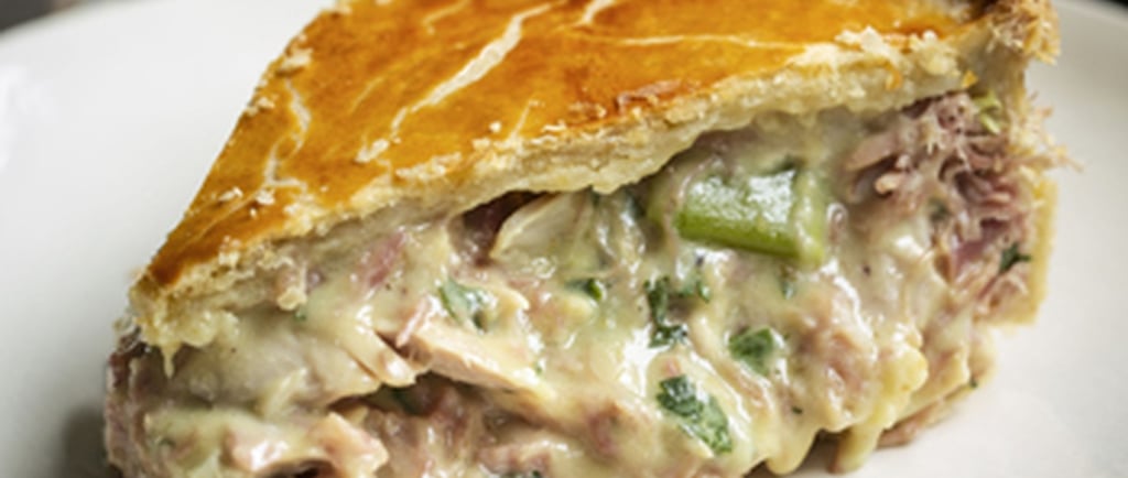 A slice of creamy chicken and leek pie with a golden flaky crust on a white plate.