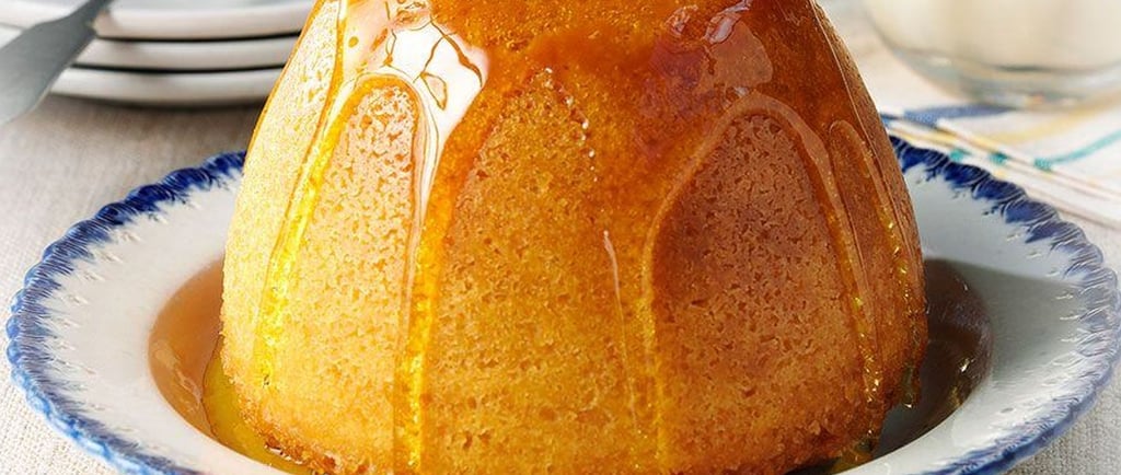 A classic golden syrup steamed sponge pudding on a blue rimmed plate with syrup drizzled over the top.
