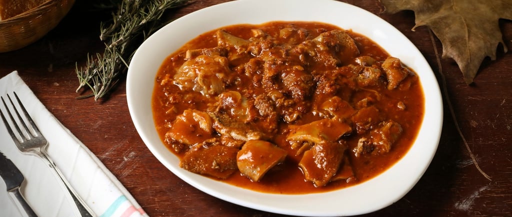 A white plate of traditional Italian tripe stew in tomato sauce on a rustic wooden table.