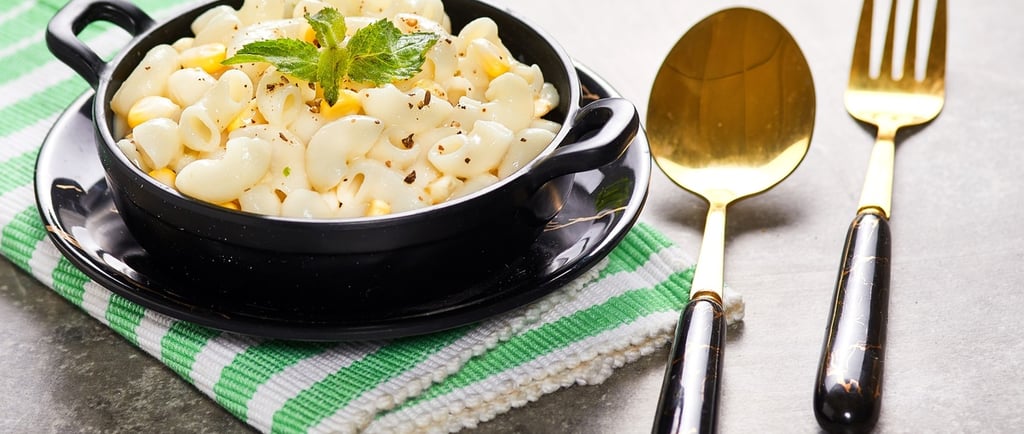 Creamy macaroni and cheese in a black bowl with a gold spoon and fork on a green napkin.