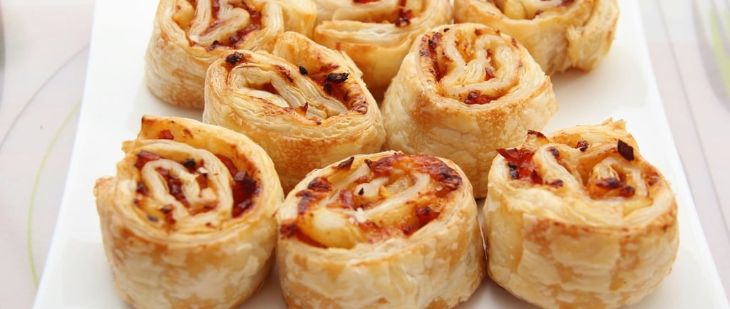 Golden brown savory puff pastry pinwheels with ham and melted cheese served on a white plate.