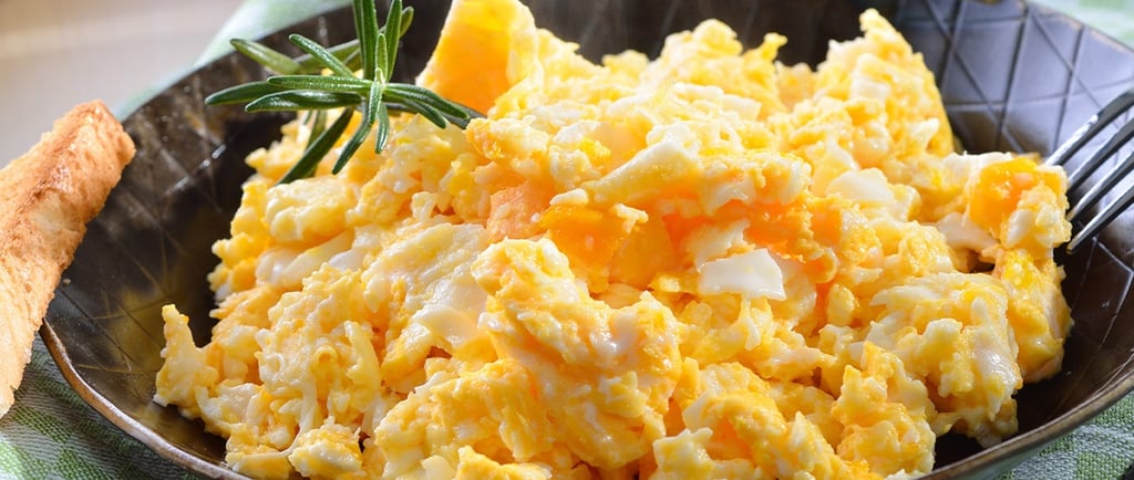 Fluffy scrambled eggs in a cast iron skillet with fresh rosemary and a side of toasted bread.