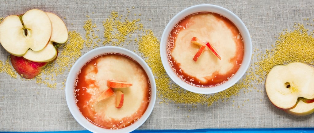 Two bowls of hot millet porridge with apple slices and sauce on a blue table.