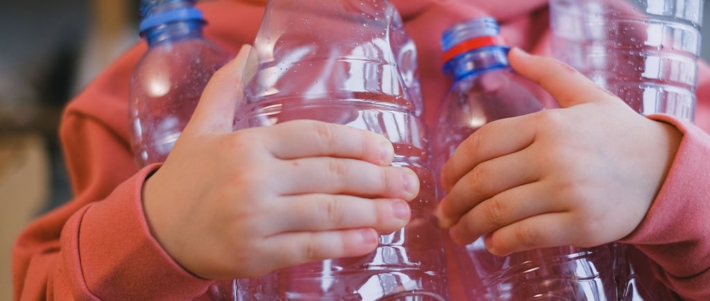 A person in a pink hoodie holding several empty clear plastic water bottles for recycling.