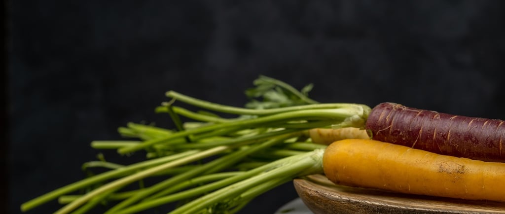 Freshly harvested heirloom rainbow carrots with green tops on a wooden plate against a dark background.