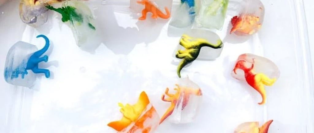 A child's hand picking up colorful toy dinosaurs frozen in ice cubes for a sensory science activity.