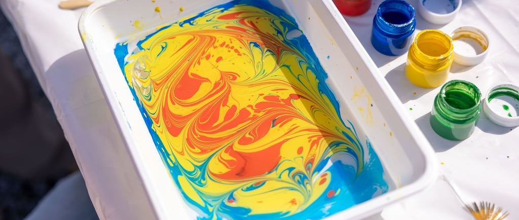 A white tray of colorful marbled paint swirled in yellow, red, and blue for ebru art.