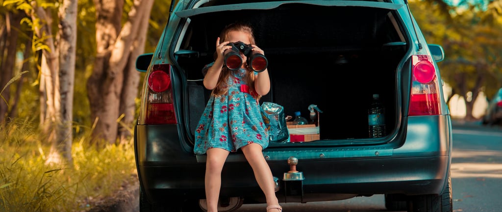 A young girl sits in a car trunk using binoculars during a family road trip adventure.
