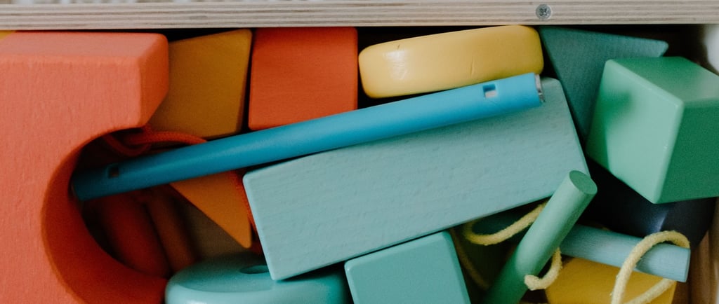 A collection of colorful wooden building blocks and geometric shapes stored in a wooden toy box.