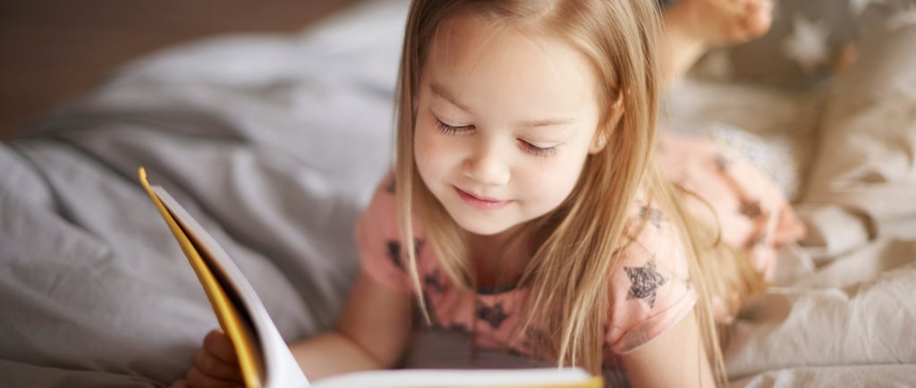 a little girl reading a book in bed