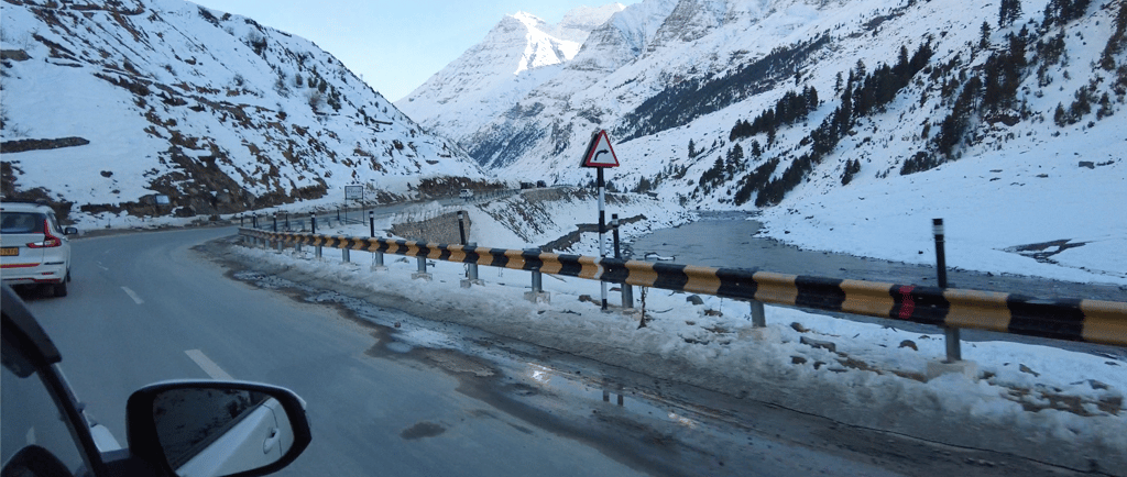 Car driving down a snow-covered mountain road from Manali to Sissu in Himachal Pradesh