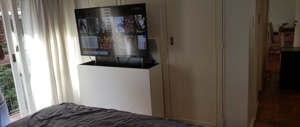 Dormitorio pequeño con mueble para ocultar TV y sistema de elevación motorizada frente a la cama