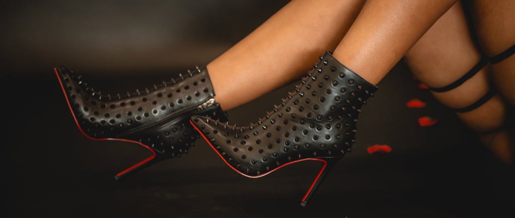 Close-up of a women's legs wearing black high-heeled ankle boots with pointed toes and decorative spikes.