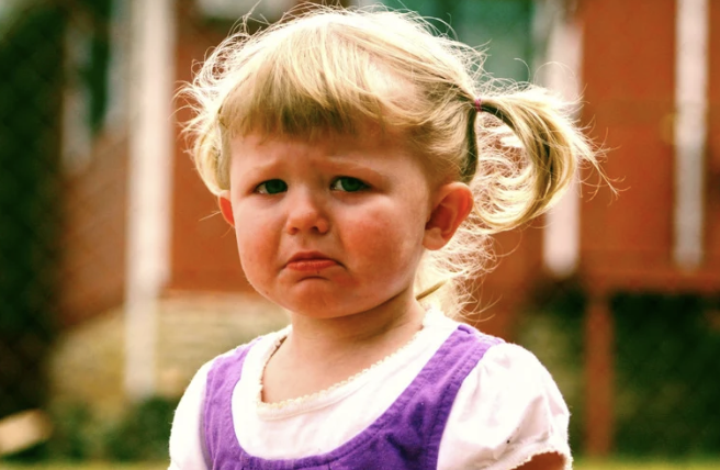 une petite fille triste et pleurant à la vue de son parent qui part du domicile