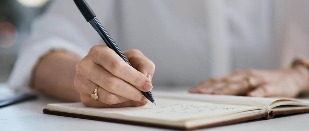 Close-up of a woman’s hand writing in an open journal with a black pen, capturing a quiet moment.