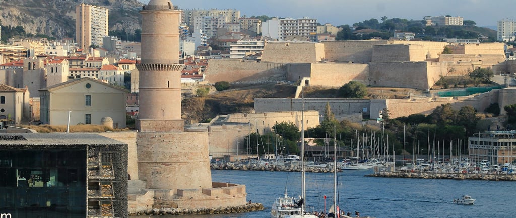 Panoramic view of Marseille Old Port featuring Fort Saint-Jean tower and the MuCEM museum building.