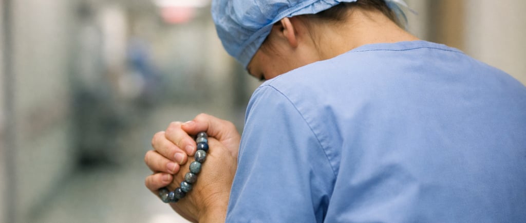 Soignante vue de dos dans un couloir d’hôpital, serrant un bracelet de labradorite.