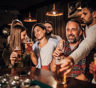 A diverse group of happy friends enjoying craft beer at a dimly lit pub during a social gathering.