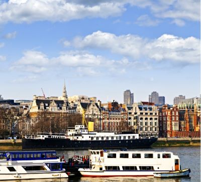 Tourist boats docked on the River Thames with London skyline architecture in the background.