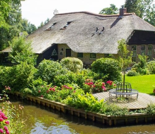 Traditional Dutch thatched roof cottage with a lush flower garden and canal in Giethoorn.