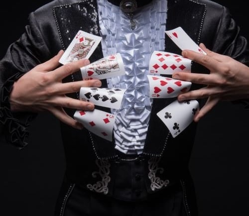 a man in a black suit and a white shirt holding playing cards